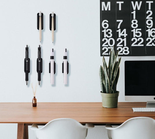Een minimalistische werkplek met een iMac, een kalender aan de muur, Verleidelijke siliconen penhouders op het bureau, een potplant en twee stoelen.