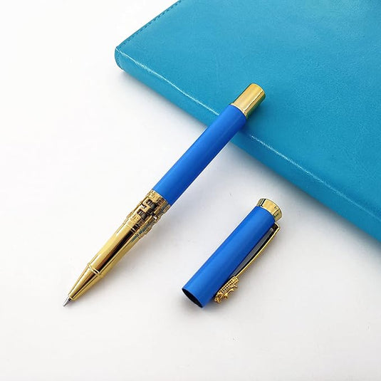 Een blauwe Een klassieke metalen rollerball voor een luxe schrijfervaring met een goudkleurige punt liggend op een wit oppervlak, naast een gesloten blauw notitieboekje waarvan de dop eraf is.
