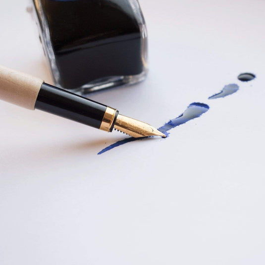 Een elegant schrijfcomfort met een duurzaam tintje van esdoornhout met blauwe inkt nabij een inktfles op een witte achtergrond.