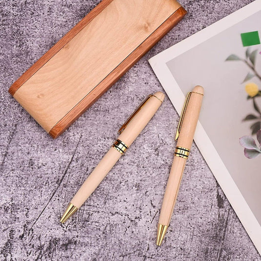 Twee houten pennen naast een bijpassend pennenetui, weergegeven op een gestructureerd oppervlak naast een digitale tablet met een bloemenafbeelding, die het perfecte cadeau voor elke gelegenheid - Het complete schrijfpakket biedt.