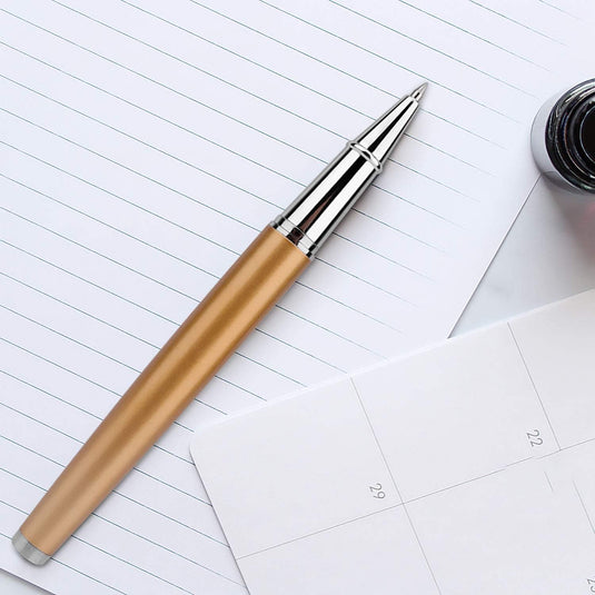 Laat een blijvende indruk achter met deze elegante en hoogwaardige rollerbalpen op een gelinieerd notitieboekje, naast een open inktfles en een kalenderpagina.