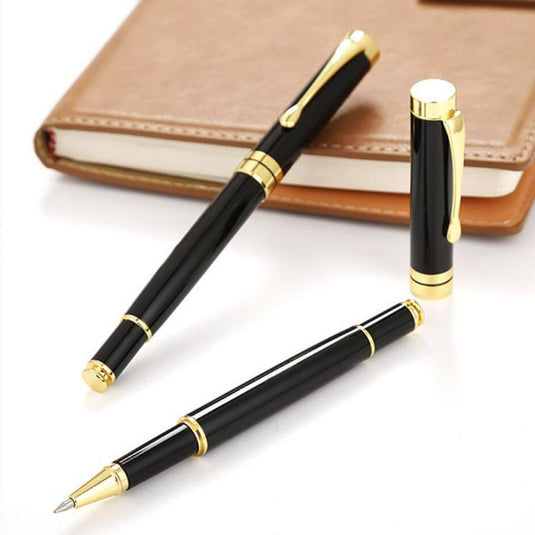 Twee zwarte en gouden Eco-vriendelijke duurzame metalen pennen liggend op een bureau naast een gesloten notitieboekje.