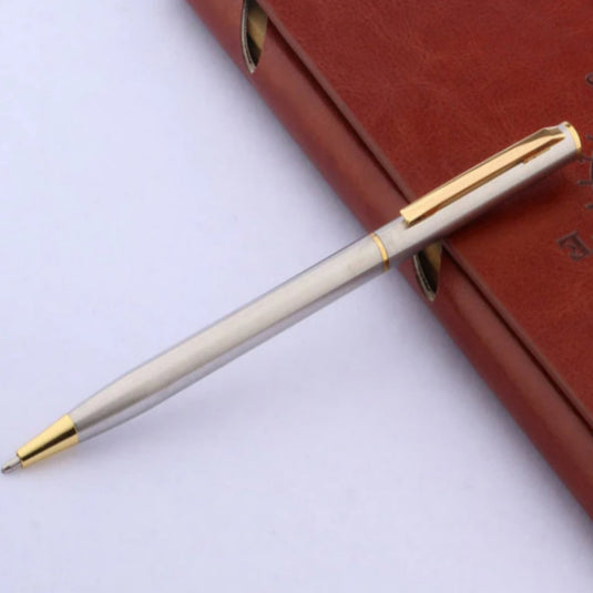 Ontdek de tijdloze elegantie van klassieke balpennen van zilver en goud roest diagonaal over een gesloten bruinleren dagboek.