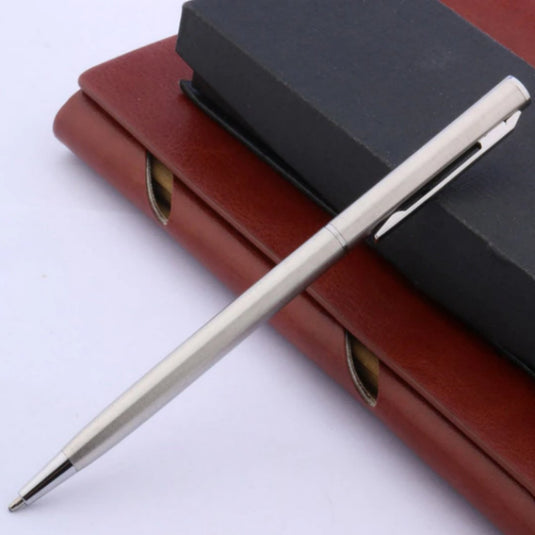 Een zilveren, Ontdek de tijdloze elegantie van klassieke balpennen, rustend op een gesloten zwart notitieboekje, dat bovenop een gesloten, in rood leer gebonden organizer ligt.