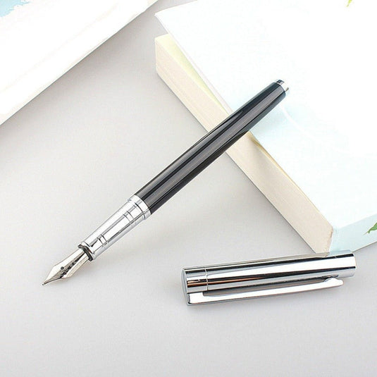 Schrijf fijn en precies met onze luxe vulpen met 0,5 mm extra fijne punt af, liggend op een bureau naast een boek.