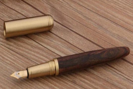 Een houten vulpen met een gouden Schrijf in stijl met de unieke combinatie van hout en koper van deze Bend Nib pen en dop, rustend op een houten oppervlak.
