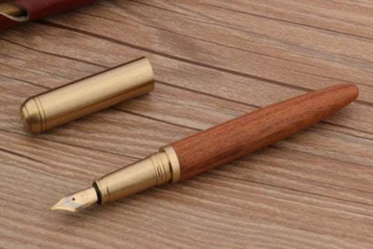 Een houten vulpen met een koperen dop en een Bend Nib, liggend op een houten oppervlak voor een unieke schrijfervaring.
Schrijf in stijl met de unieke combinatie van hout en koper van deze Bend Nib pen.