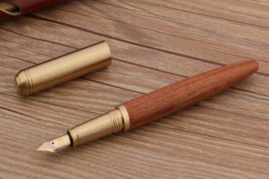 Schrijf in stijl met onze unieke Schrijf in stijl met onze unieke houten en koperen pen met F-nib op een houten tafel.