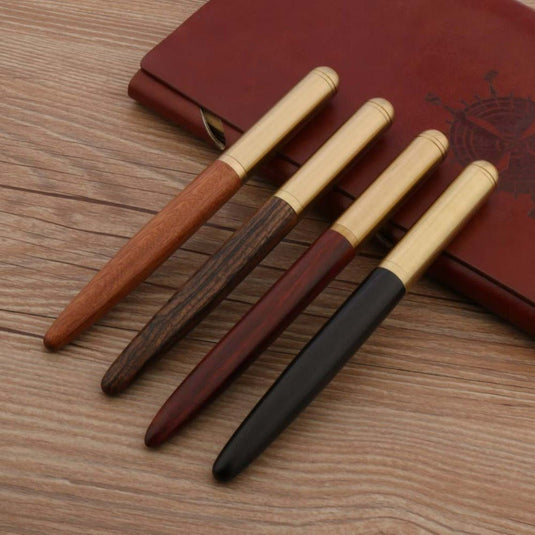Vier Schrijf in stijl met onze unieke houten en koperen pennen met F-punt gerangschikt op een houten oppervlak voor een gesloten leren dagboek.