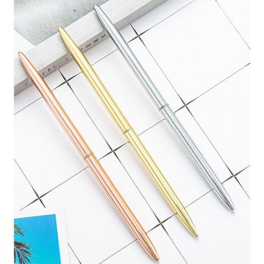 Drie elegante zakelijke metalen balpennen in roze goud, goud en zilveren kleuren, georganiseerd diagonaal over een planner met een rasterontwerp.
