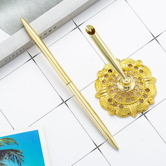 Een gouden Schrijf met stijl en professionaliteit met deze elegante zakelijke metalen balpen- en pennenhouder met een filigraan ontwerp geplaatst op een witte ondergrond, naast een notitieboekje en een foto met een palmboom.