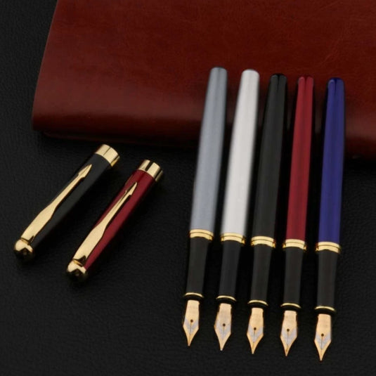 Een verzameling elegante Schrijf soepel en elegant met onze metalen zakelijke vulpen met gebogen penpunt naast een bruinleren dagboek op een donker oppervlak.