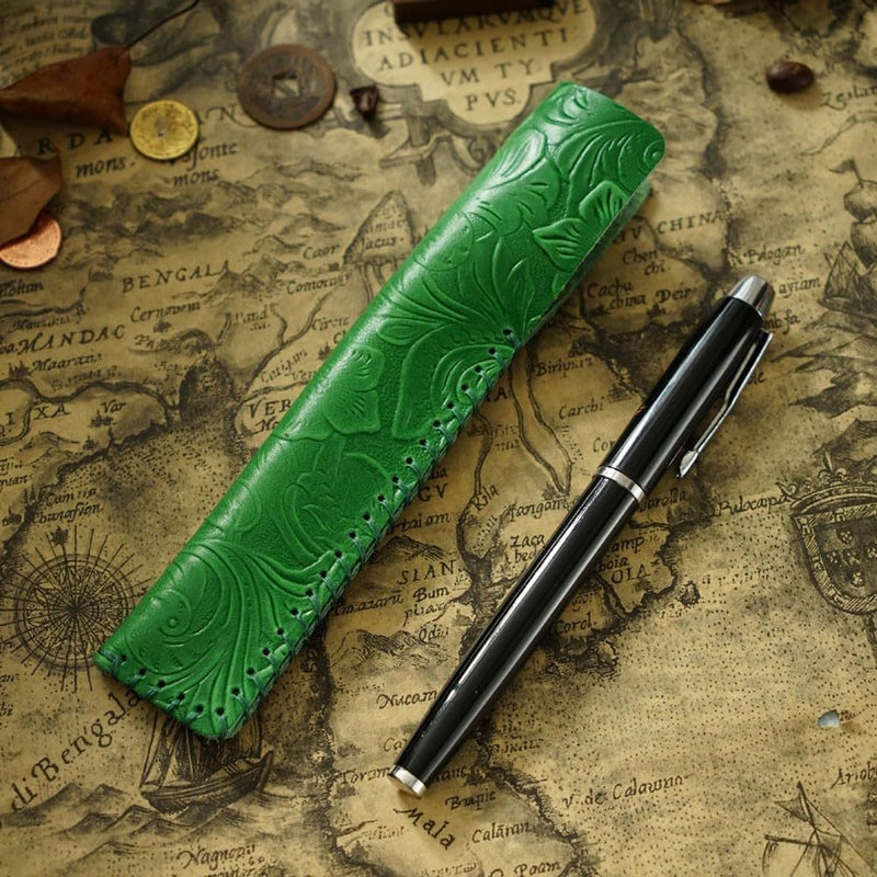Laad afbeelding in Galerijviewer, Een groene vintage lederen pennenhouder met reliëf en een zwarte vulpen op een antieke kaartachtergrond.

