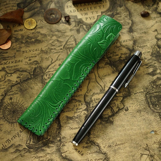 Een groene vintage lederen pennenhouder met reliëf en een zwarte vulpen op een antieke kaartachtergrond.